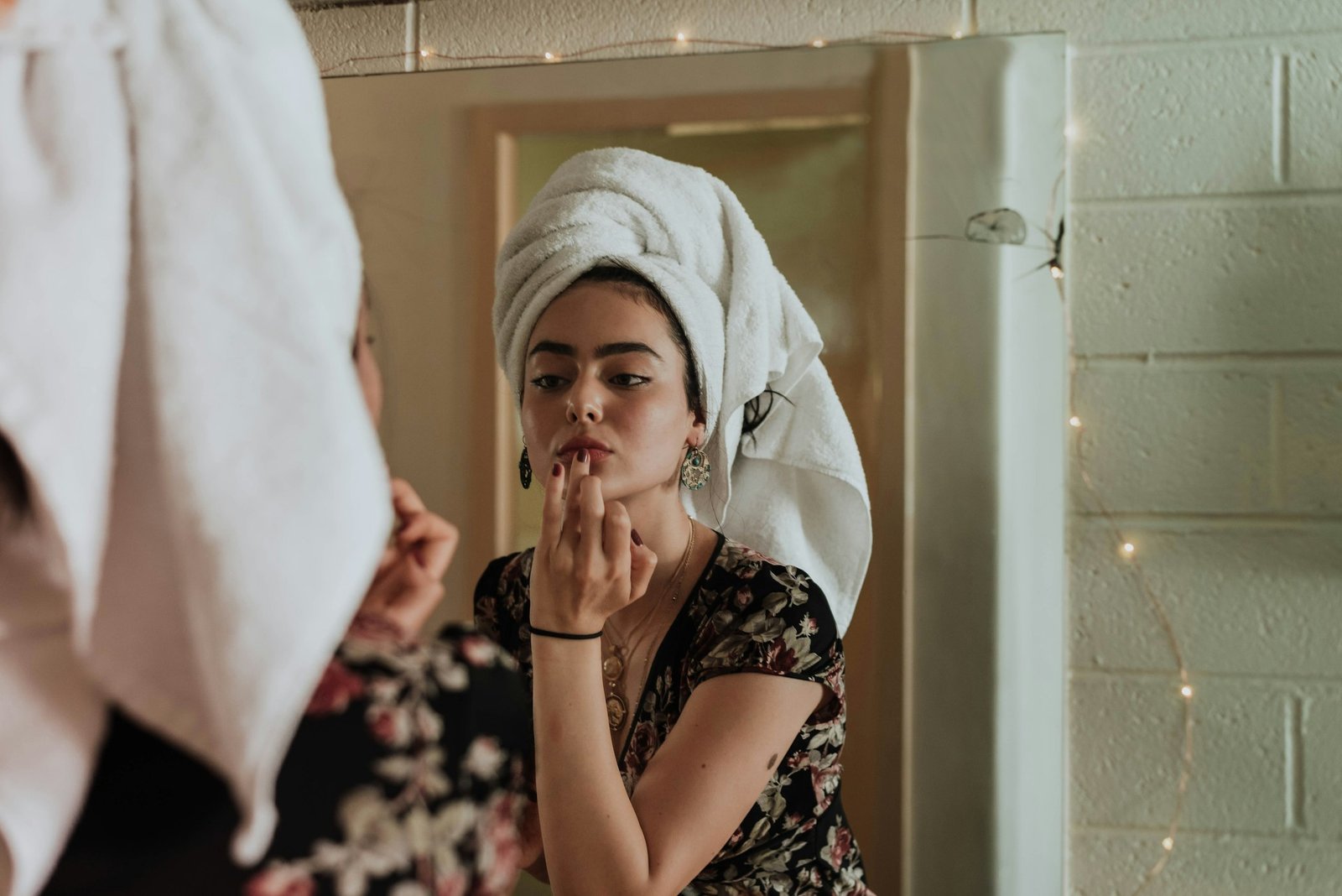 Mulher com toalha no cabelo se olhando no espelho depois do banho